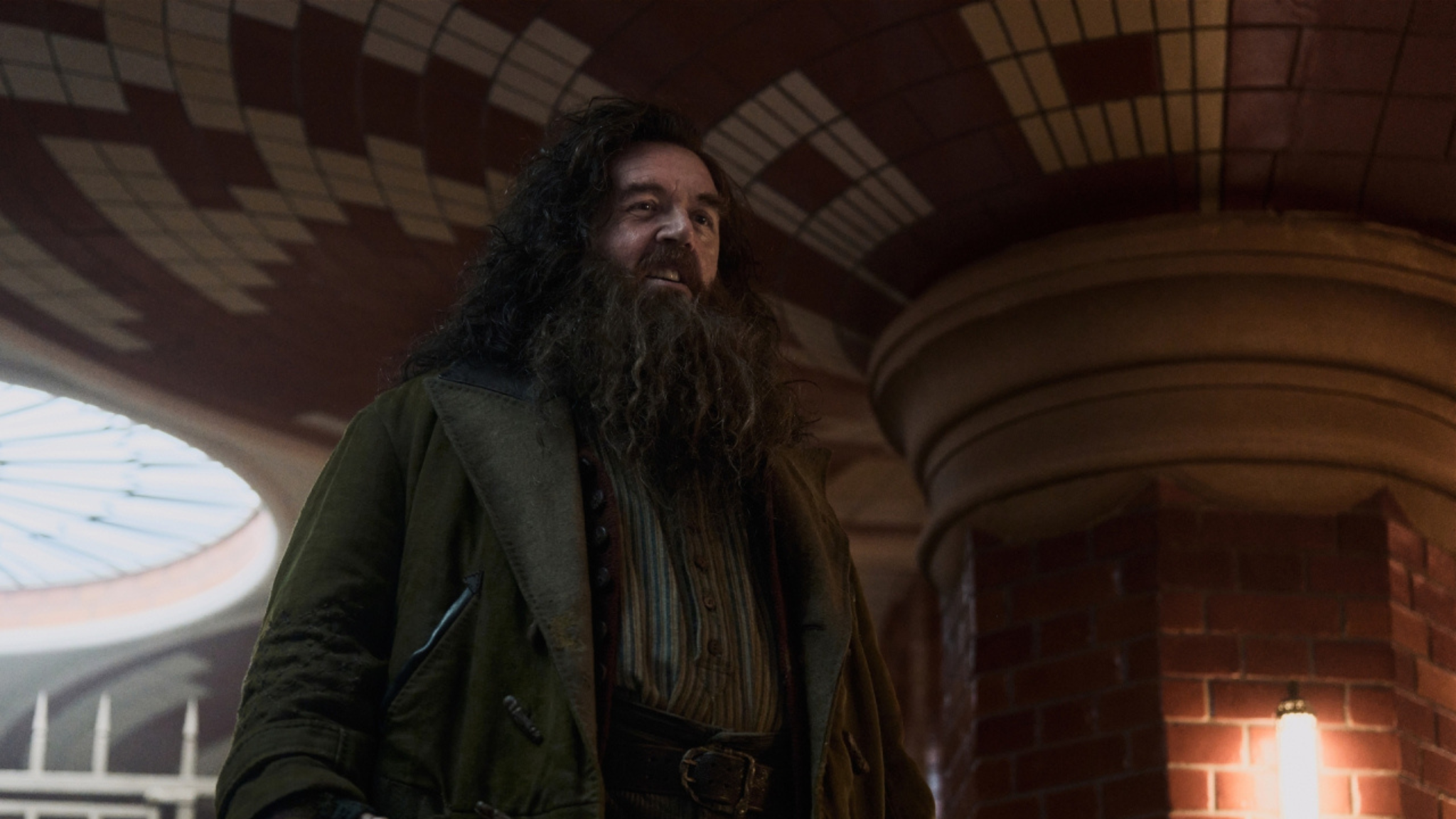 Nick Frost as Rubeus Hagrid in HBO's Harry Potter series, standing in a brick-vaulted hall in a heavy coat.