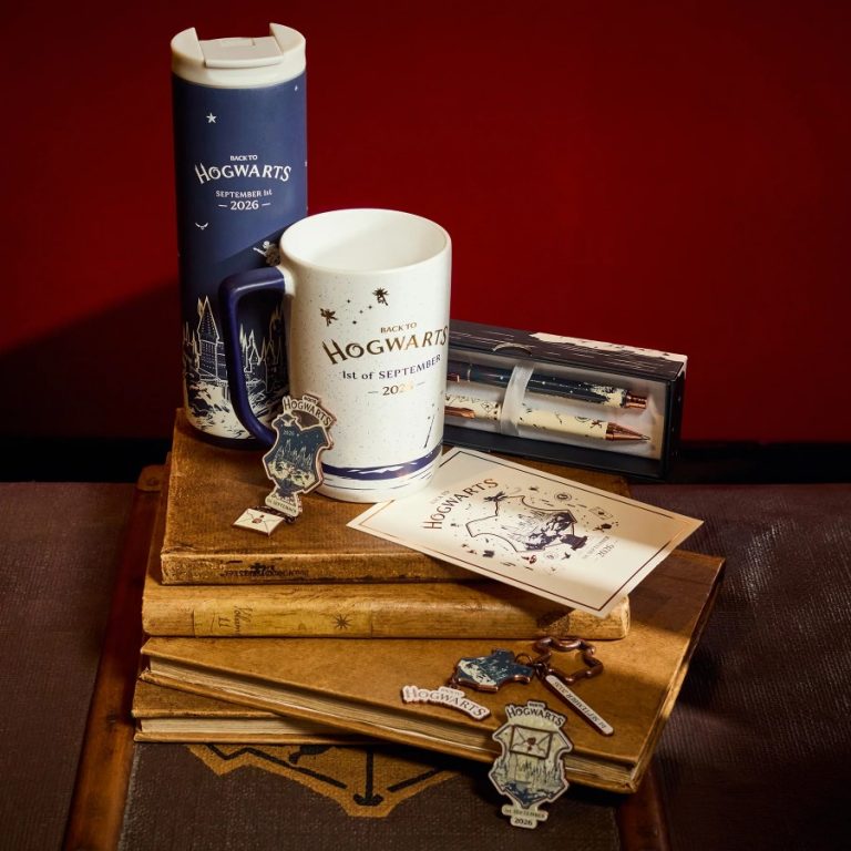 The Back to Hogwarts 2026 collection arranged on old books, including the navy water bottle, ceramic mug, pen and pencil set, postcard and charms