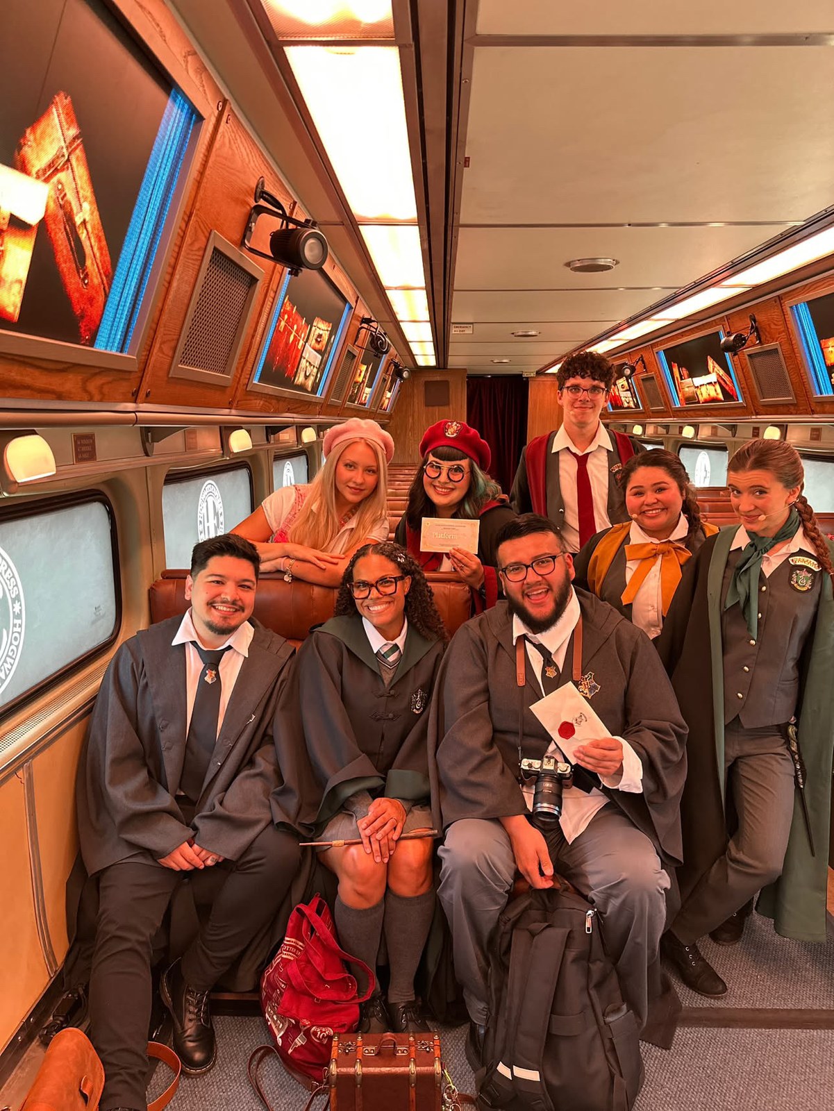 Interior of a Hogwarts Express carriage with performers and guests, screens lining the walls