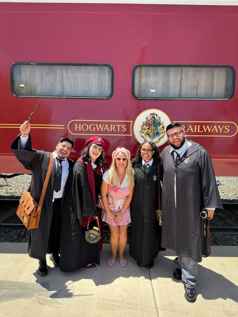 Guests in Hogwarts robes outside the Hogwarts Express train before boarding